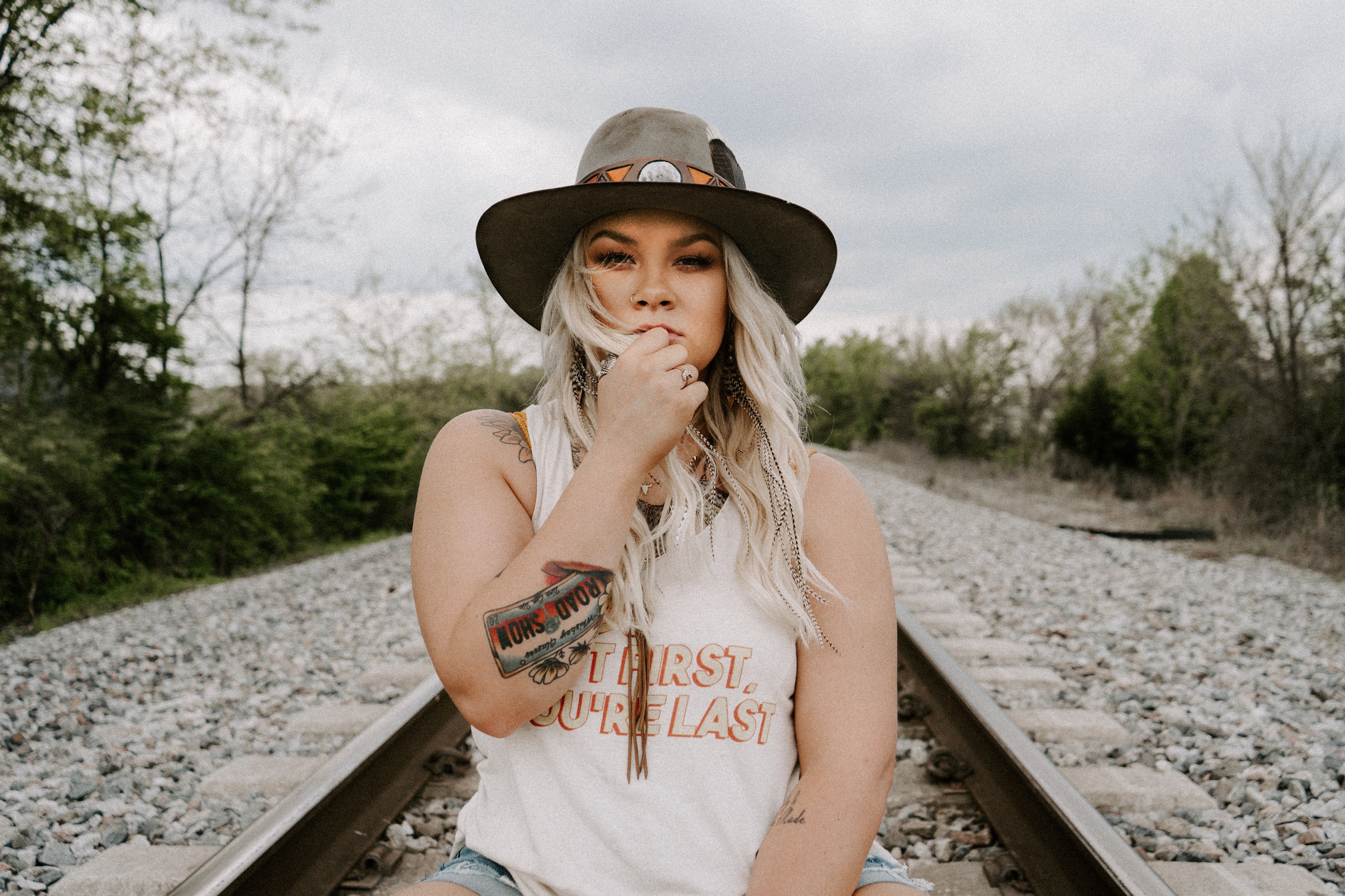 Ashland Craft in between railroad tracks wearing a white tank top and a cowboy hat.