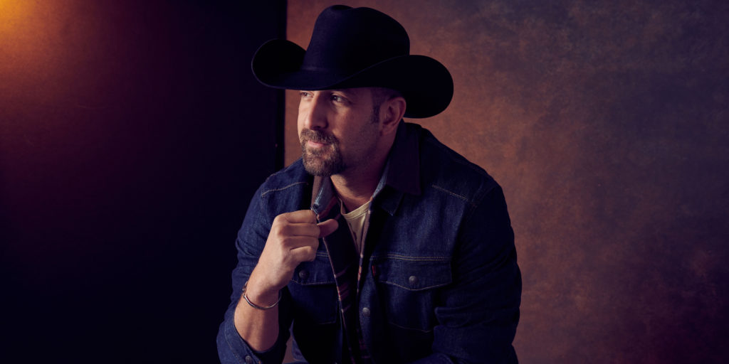 Buckstein sits while wearing a denim jacket and cowboy hat