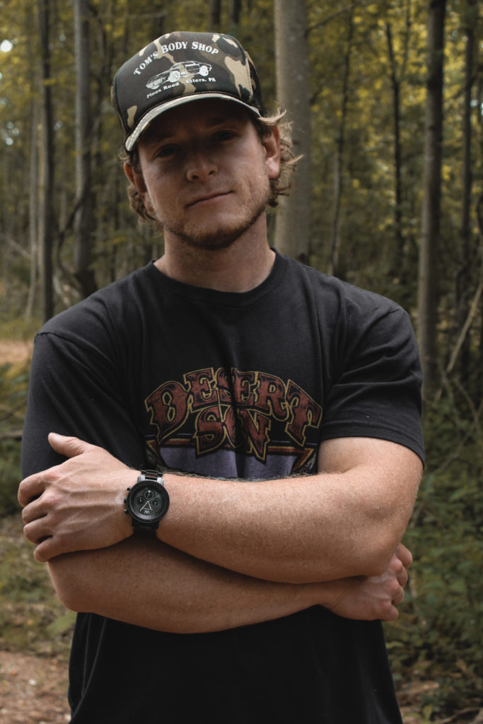 Connor Manley stands in the woods while wearing a ball cap