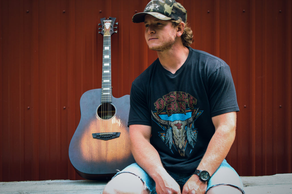 Connor Manley with his guitar wearing a camo ballcap.