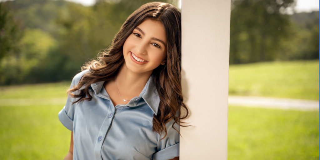 Jordana Bryant, New Country Artist to Watch, leaning against a wooden post in a green field