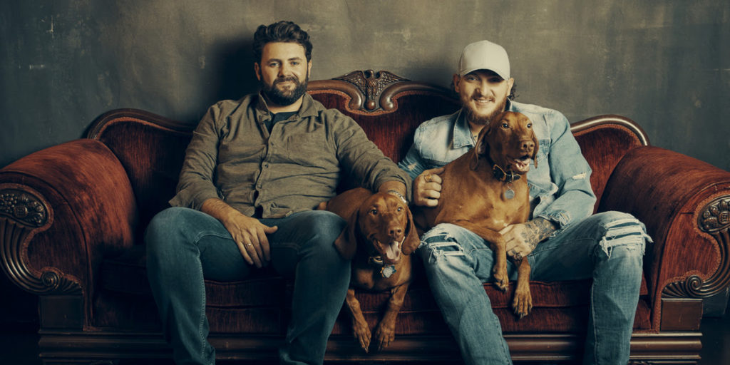 Pryor and Lee sit on red couch with two brown dogs